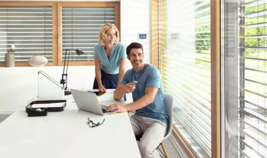 Ein Mann sitzt am Tisch und steuert seinen Rollladen per Fernbedienung