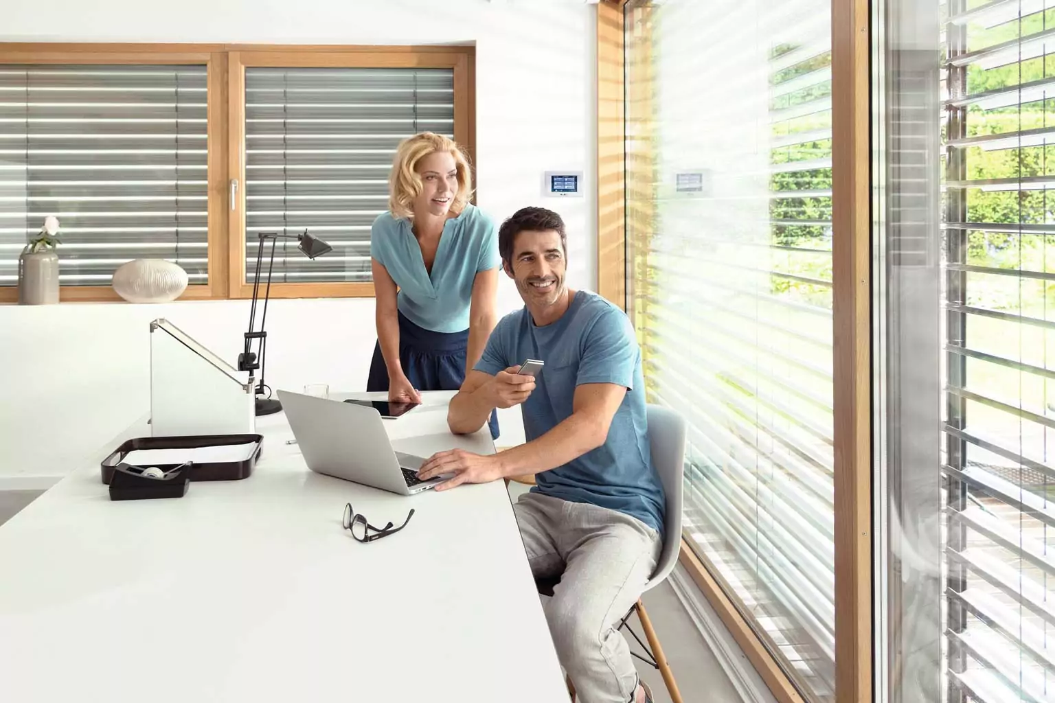 Ein Mann sitzt am Tisch und steuert seinen Rollladen per Fernbedienung